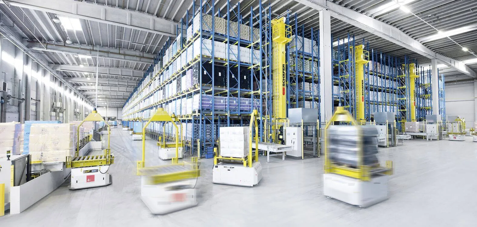 Automated guided vehicles moving pallets down the aisles of a high bay warehouse