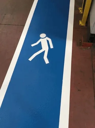 Blue pedestrian walkway with a walking figure marked on a factory floor