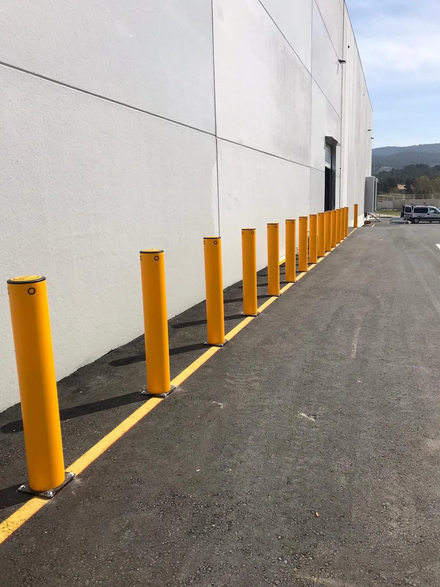 Reihe gelber Poller entlang der Außenwand einer Industriehalle an einer Zufahrt