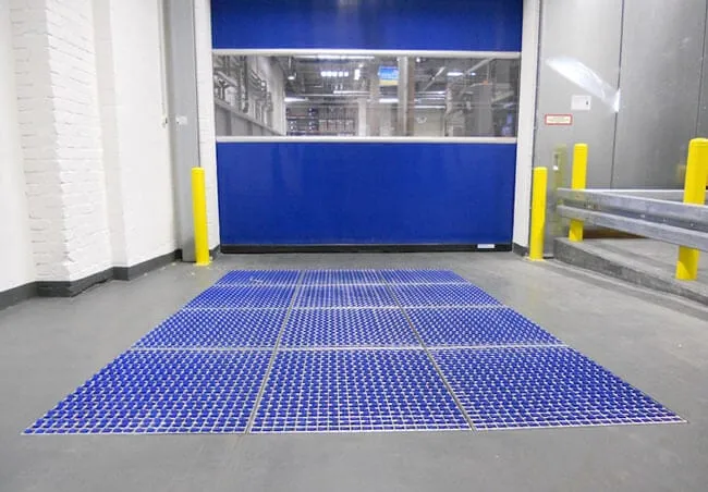 Blue brush cleaning field laid across the floor in front of a roller shutter door