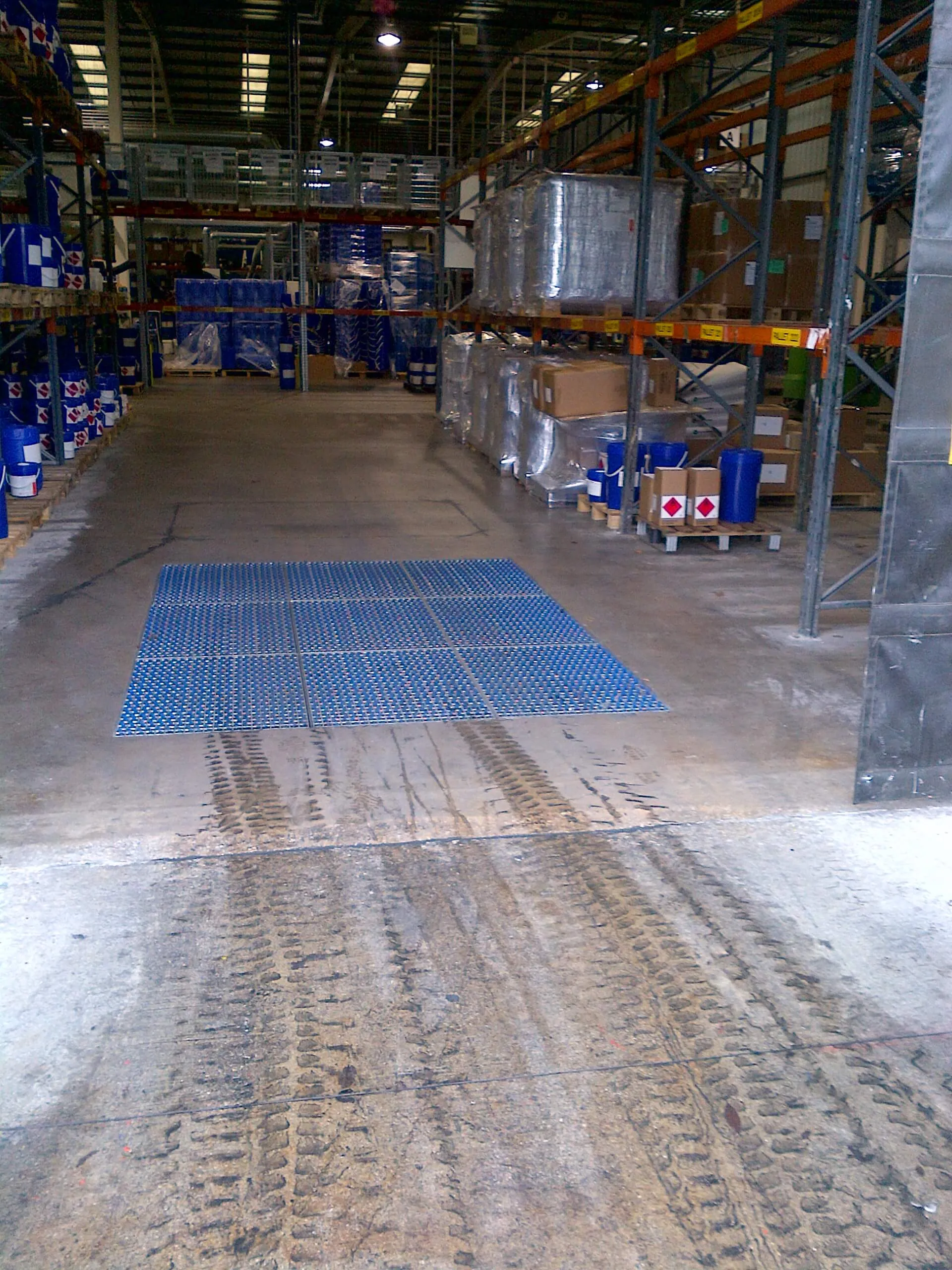 Brush cleaning field in a warehouse aisle with tyre marks running away from it across the floor