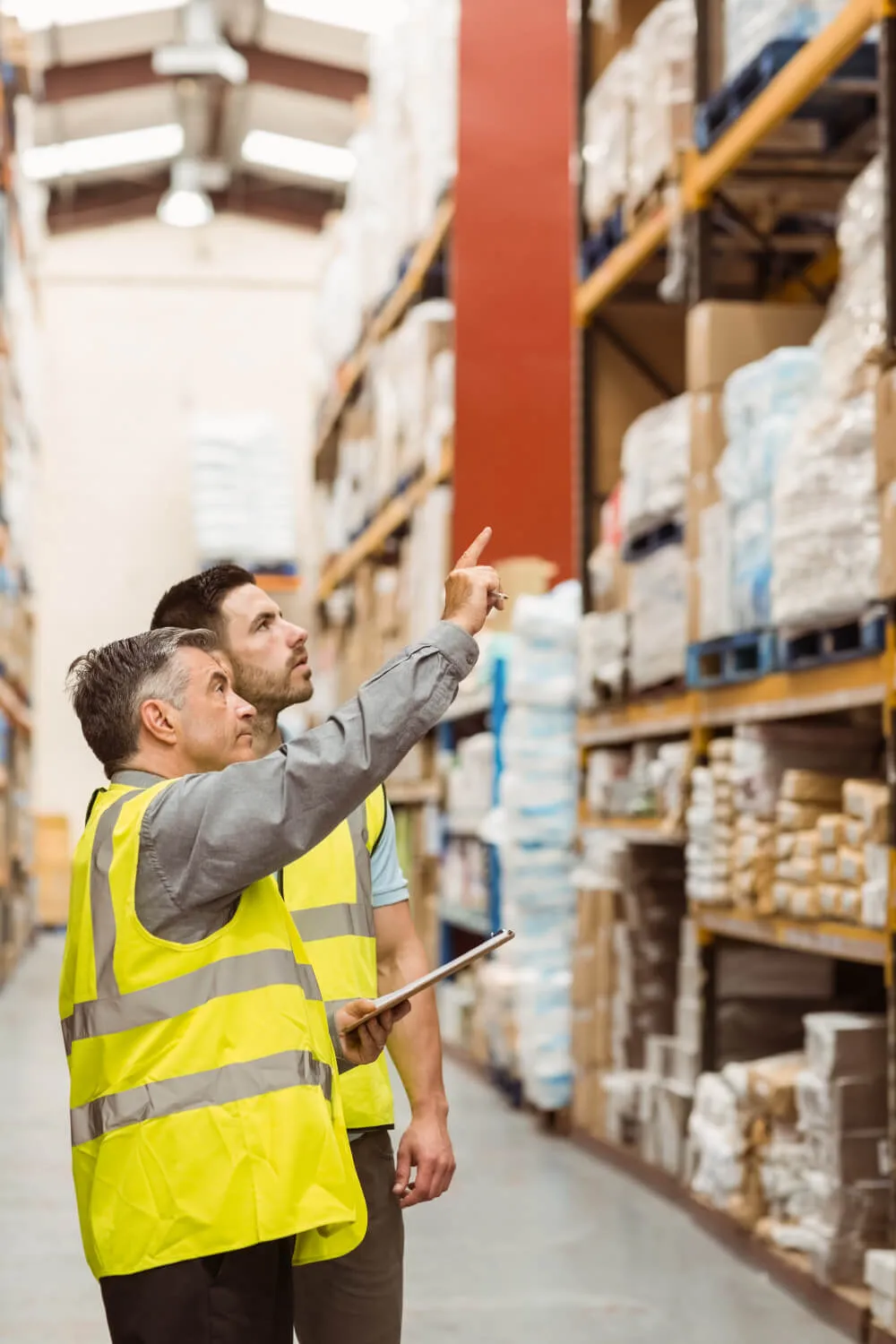Consultant and warehouse manager looking up at a racking run while reviewing notes on a clipboard