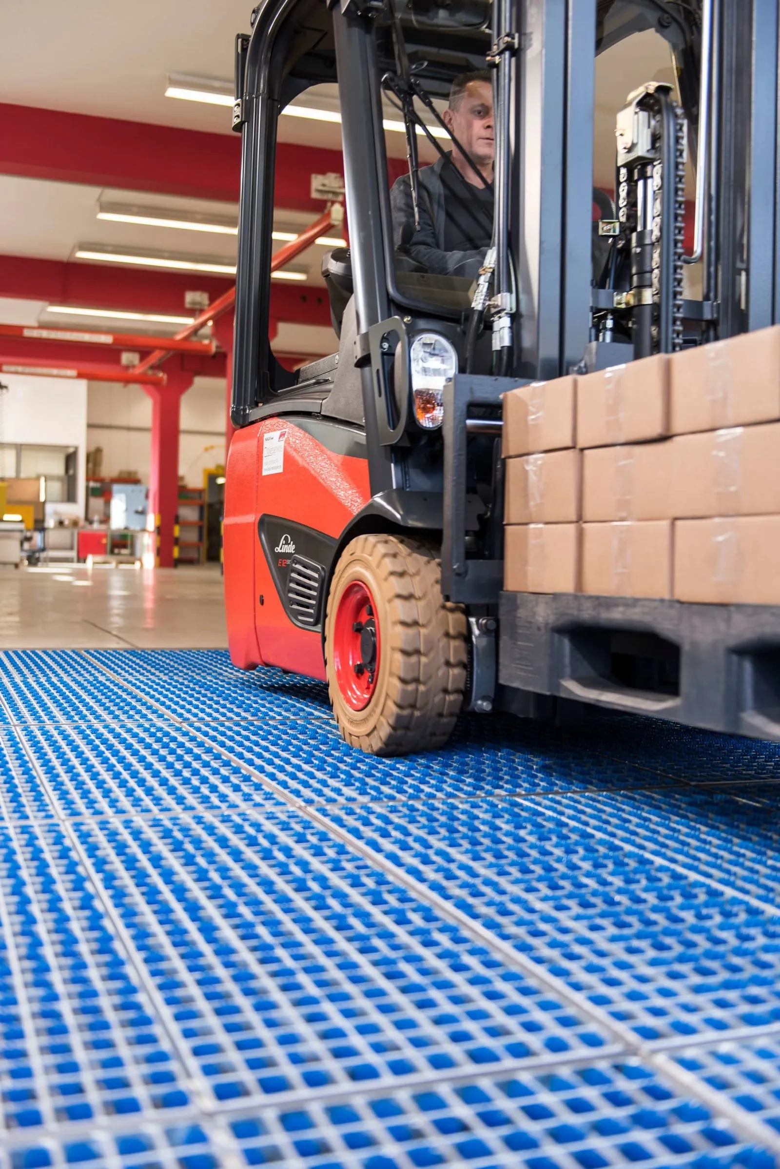 Loaded forklift driving over a blue brush cleaning field laid flush into a warehouse floor