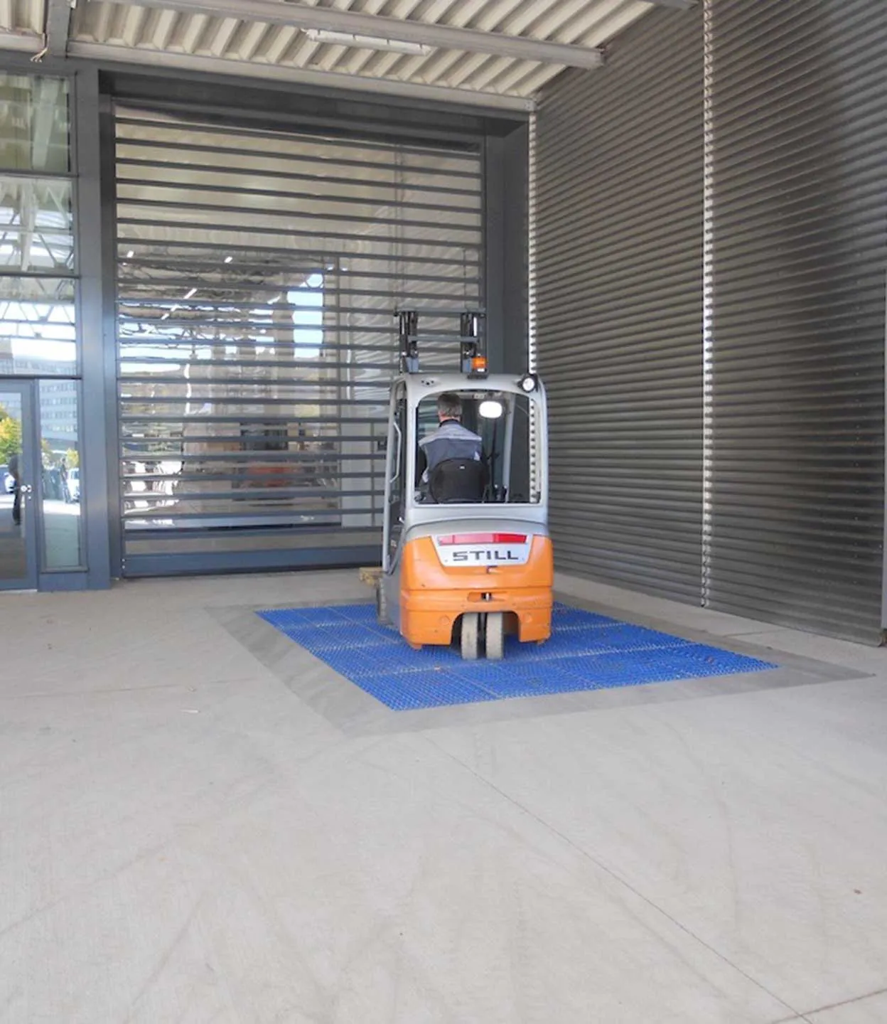 Forklift driving in through a roller shutter door and over the cleaning field laid into the floor