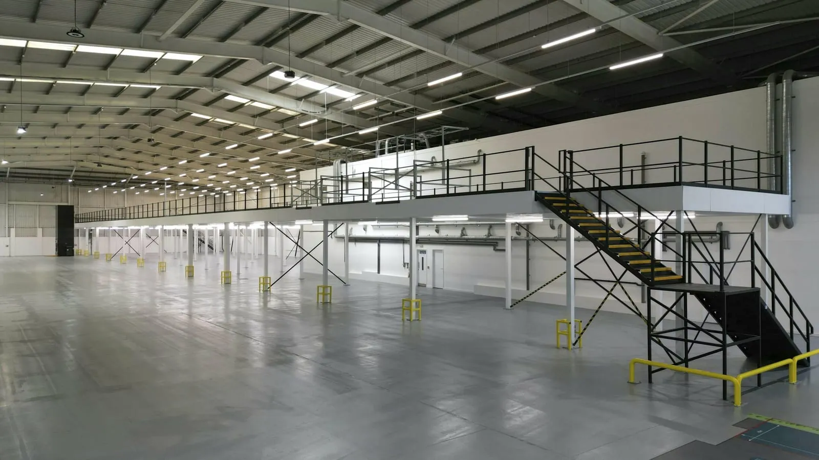 Steel mezzanine floor with a staircase running along the wall of an empty warehouse unit