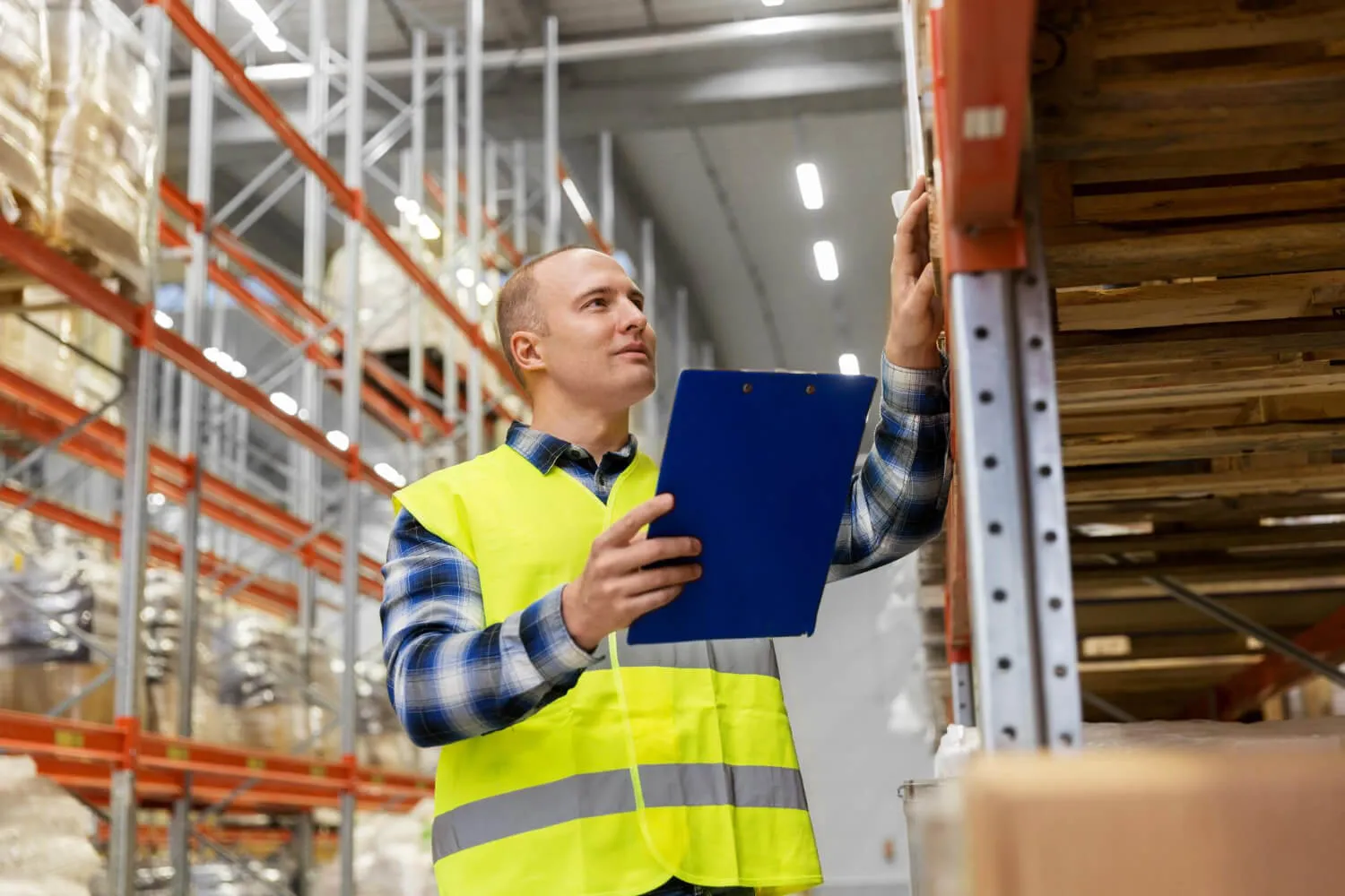 Inspector in a hi-vis vest checking a beam connector at eye level with a clipboard in hand
