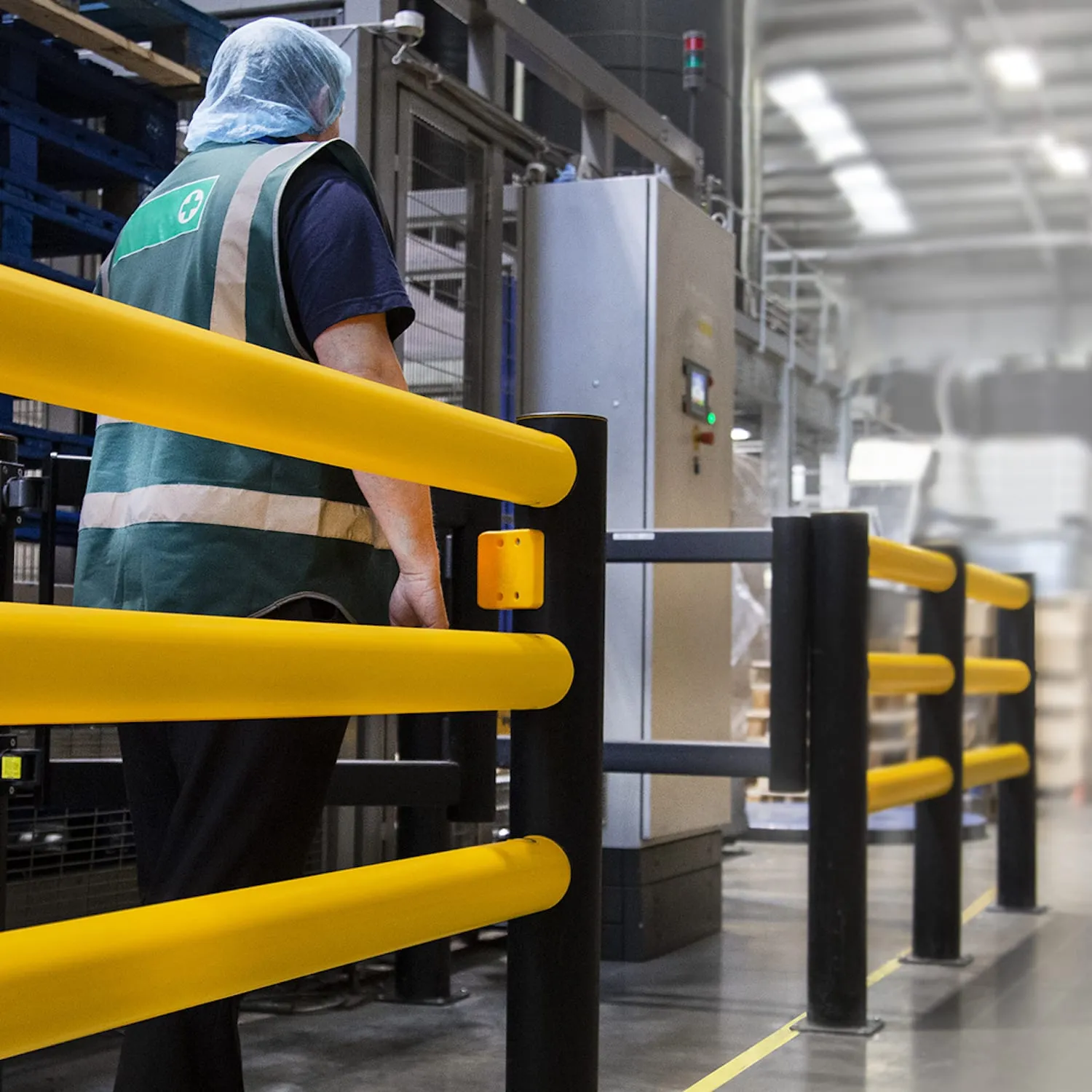 Yellow safety barrier separating a walkway from a machine where an operator is working