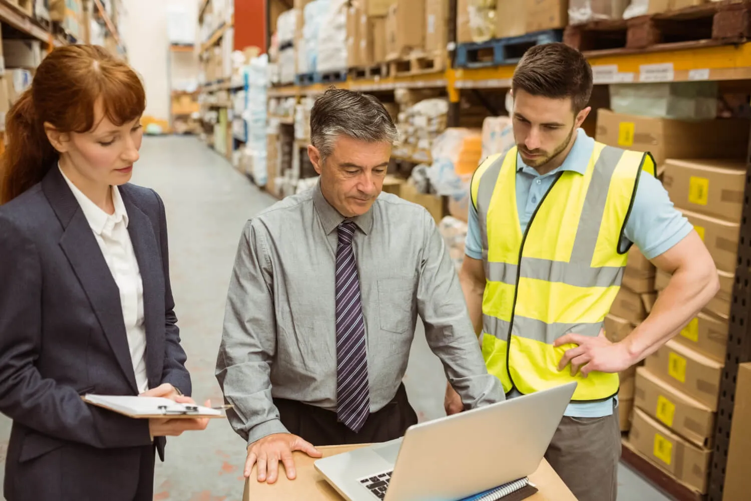 Three colleagues reviewing figures on a laptop on the warehouse floor