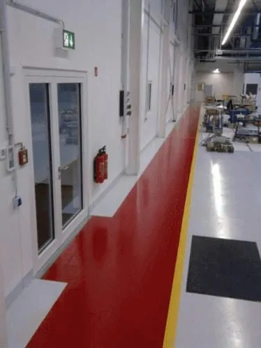 Rot beschichteter Gehweg unter einem grünen Rettungszeichen an einer Fluchttür