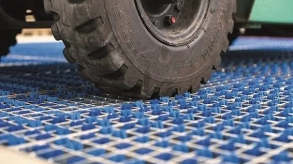 Wiel van een heftruck rijdt over een blauw borstelveld, gezien vanaf vloerhoogte