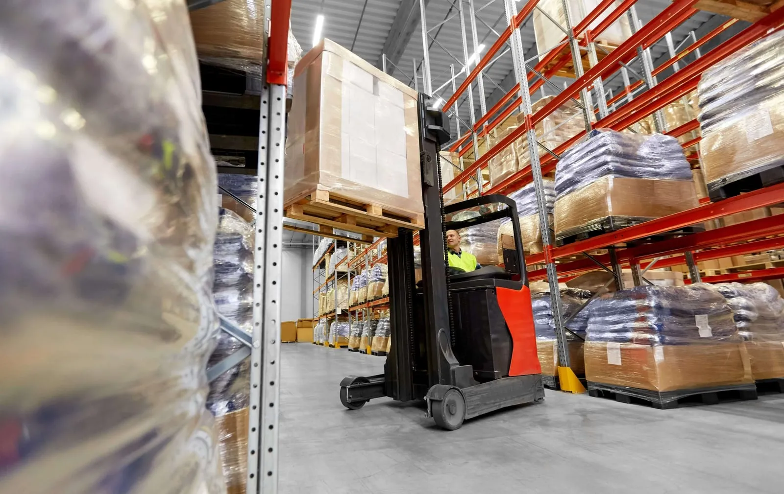 Reach truck lifting a pallet high into a narrow aisle between loaded pallet racking runs